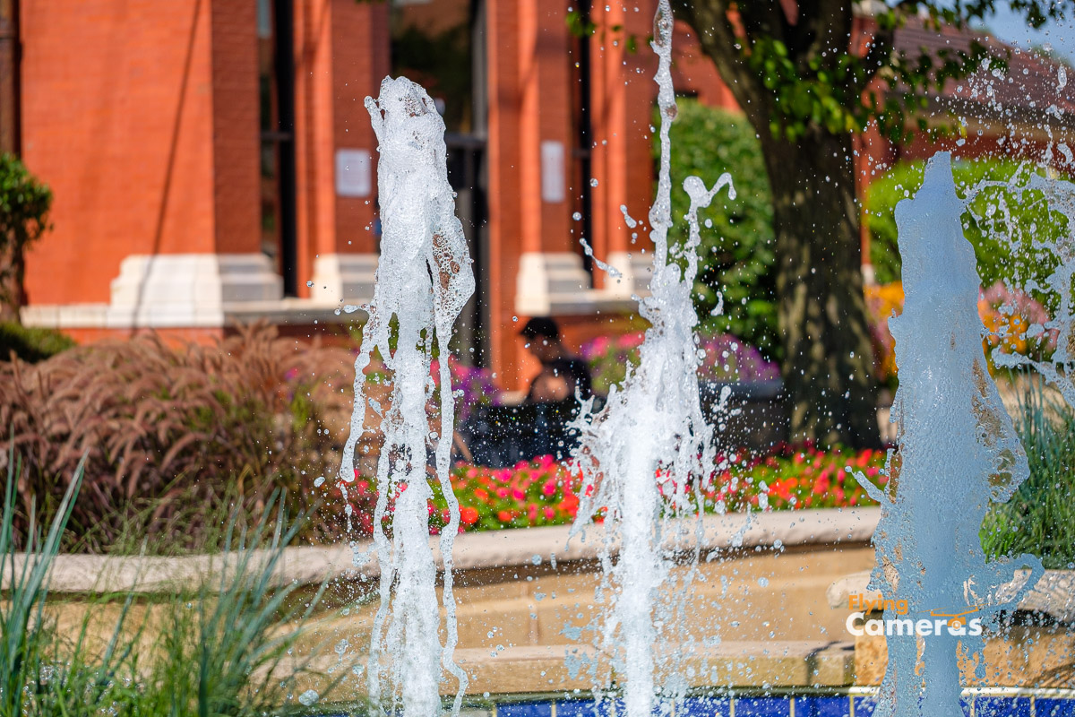 Resident sitting on bench in municipal park framed by water spouts from fountain